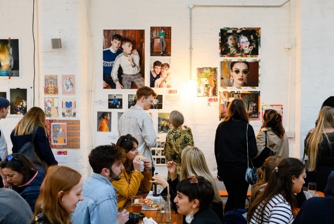 Adults in a group setting, some seated with food and some looking at photographs on the wall